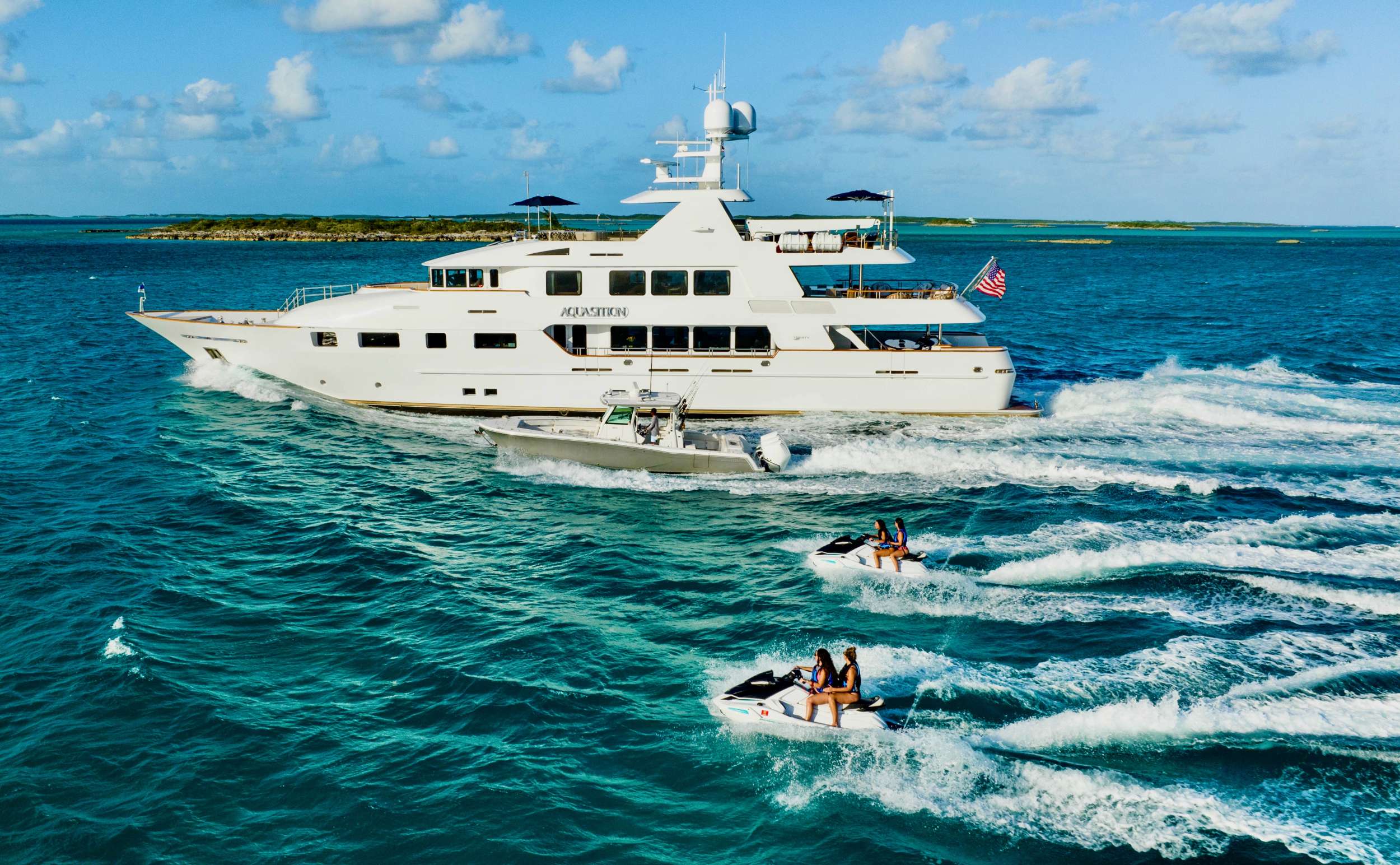 Aquasition, a 142’ Trinity yacht whose spectacular interior features cherry wood joinery with
maple burl inserts throughout. She has zero speed stabilizers and a shallow draft for her size making her and excellent Bahamas and New England cruising choice. Her owner has enjoyed decades of charter yacht ownership and upon purchase; they completed an extensive refit to ready her for charter. The complete interior was updated as well as exterior improvements, additions, and many audio-visual upgrades. The flybridge was designed and reconfigured specifically for charter guest’s enjoyment. There is a beautiful Jacuzzi area as well as sun beds, full bar and entertainment as well as aft lounging area with umbrellas for shade and total relaxation. Below the flybridge on the sky lounge deck there is a massive round table for dining and comfortable furniture aft for lounging. The sky lounge is a comfortable and happy space and offers a game table, the perfect spot for movie watching and full bar. The main salon features formal dining forward and aft salon area that includes an entertainment system. Aft of the salon is a spacious deck area with dining option and access to the expansive swim platform. Underway the 2 wave runners are stored here and once at anchor they are in the water along with an extensive list of other toys and ready to go for guest’s enjoyment.