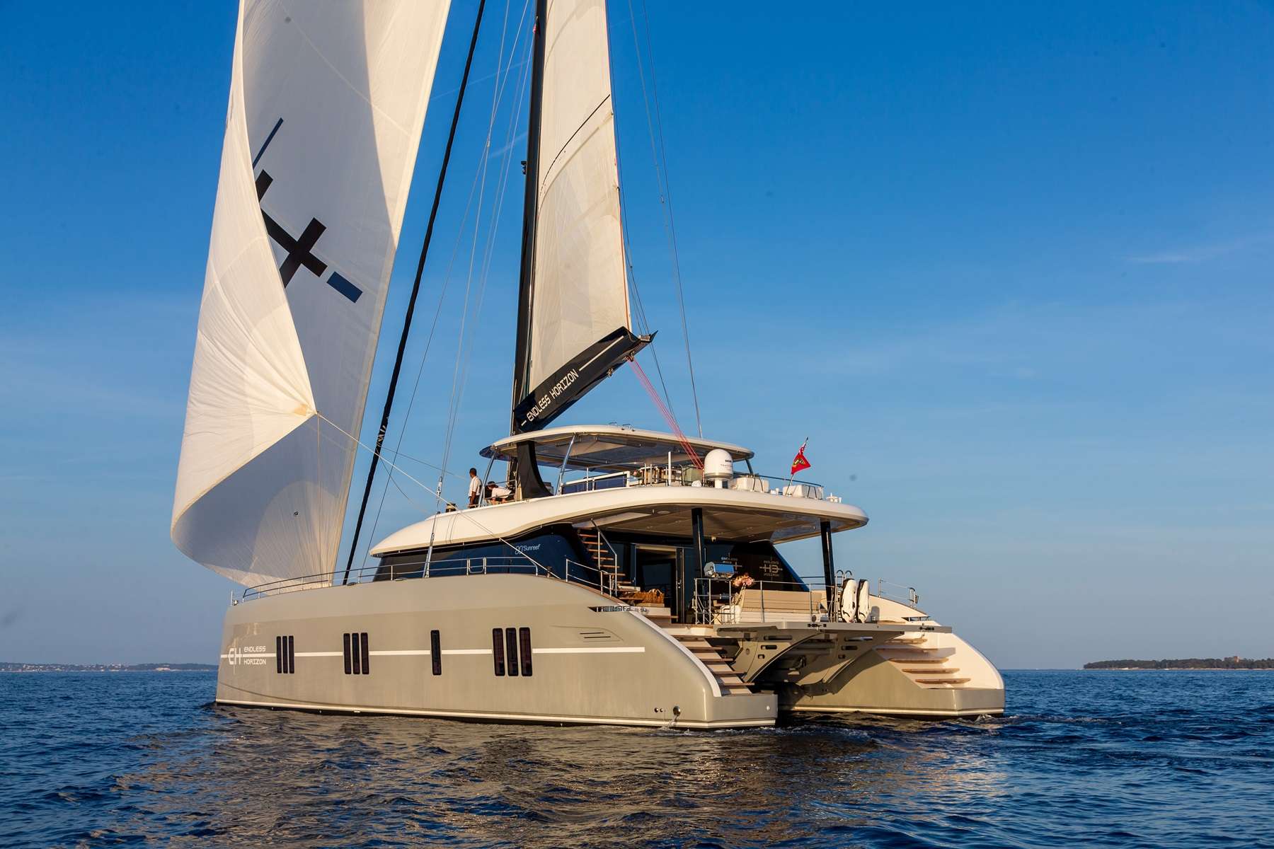Launched in 2022, Endless Horizon was designed and built by Sunreef. ENDLESS HORIZON 80, is a lavish sailing catamaran, an ideal getaway for those seeking luxury, comfort and adventure. Endless Horizon has 4 guest cabins, 1 king-size and 3 similarly sized queen-size cabins, accommodating up to eight guests.
This yacht is known for it’s immense freeboard, which lends space to all living areas. Endless Horizon boasts over 3650 square feet of living space, with a central open-plan galley on the main level with a large living room fitted with a cozy couch and 360 degree views of the water around you. Elegant, uncluttered, and minimalist, with a focus on large windows, natural materials, and neutral colors. This custom designed yacht is nothing short of luxury.
Endless Horizon has a walkthrough design allowing you to walk easily from the aft cockpit dining area, through the saloon to the bow alfresco. Fitted with a removable shade this is a perfect area to lounge in comfortably. The bow is fitted with two large trampolines, giving this vessel the traditional catamaran feel.
There is a large dining table on the aft alfresco area with a fully stocked wet bar as well as a daybed. Just off the back of the aft dining area is a large hydraulic platform which is where the tender is launched from. The tender, is equally specked with a fusion stereo system, underwater lights, courtesy lights and navigation system. Perfect for daytime tender excursions. The tender platform doubles as a water toy area during the day, where we can launch the seabobs and e-foils or even set up a day lounge for sunbathing and cocktails.
The spacious flybridge is fitted with dual helms, a day bed, additional sun awning, wet bar and a large dining table if you choose to dine up top. All sailing lines lead to the base of the mast, an ideal spot for guests to join in on the sailing action.
On the lower level you will find 4 very well appointed cabins, with their own ensuite, high end finishes including rainfall showers, spacious closets and a TV in each. With comfortable beds fitted with top quality hotel bedding, you can slip into bed each evening with an ocean view looking through Sunreef’s signature vertical windows.