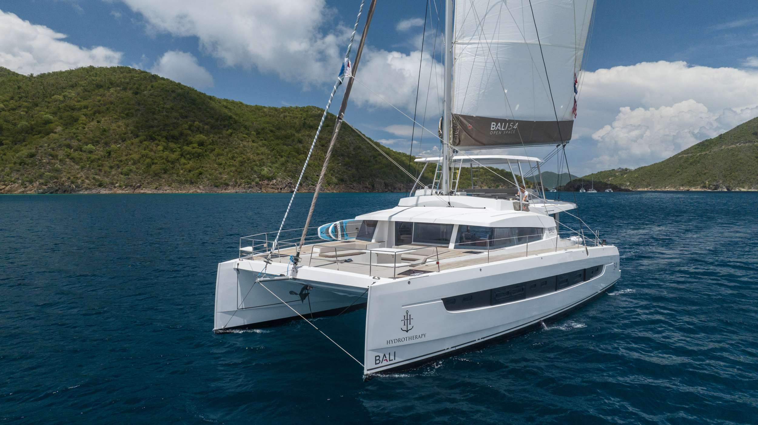 The Bali 5.4 is a “Multihull of the Year” award-winning catamaran. The design was new to the market in 2019 and provided a fresh approach to sailing. It is revolutionary in how space is accessed, with deliberate attention to flow and open space and it succeeds in producing a scale that feels less like a boat, and more like an upscale floating condominium.

Bali catamarans are known and appreciated for their unparalleled success in blending luxury, space, and performance; producing a sailing experience that is unparalleled. This new design further capitalizes on that reputation with the advent of the “Bali garage door” that is the centerpiece of the yacht. It allows for the aft wall of the yacht to simply disappear, opening up the back of the yacht to an unobstructed view of paradise. This also affords indoor/outdoor dining options and gives the ever-present Caribbean breeze ample opportunity to make its way through the yacht with ease.

With her solid foredeck gone are the forward trampolines, replaced by a large relaxing lounge area complete with cushions for sunbathing. A full-sized door provides access directly from the lounge area into the salon, allowing free movement through the yacht. A walk up to the flybridge unveils a seating area perfect for cocktails and taking in sunsets. There is also another area for sunbathing on the flybridge where you can take in the sights of the islands from the highest vantage point on the yacht.

The Bali open space design is further complemented by the superior outfit and aftermarket items available on Hydrotherapy. No detail has been left unnoticed from the fine linens, pillows and throws to the wine glasses, serving and flatware that make every day feel luxurious. She has been stocked full with every appliance and kitchen accessory to allow the chef to fully showcase the mastery of their art. And the water toys abound, allowing guests to fully experience all the Caribbean has to offer, both in and out of the water.

Hydrotherapy will accommodate 8 charter guests in 3 spacious queen cabins and 1 sprawling master cabin for those who desire more space. She is a brand new 2023 sailing catamaran with full teak spanning the entire the yacht, wine fridge, solar panels, air conditioning, water maker, ice maker, full sized refrigerator, a fully customizable menu, Caribbean made ecofriendly and reef safe toiletries, a bar stocked to guest preference, coffee/espresso machine, rendezvous scuba diving, snorkeling gear, underwater scooters, wake surfboard, 2 stand up paddle boards, 10 ft. floating dock, pool noodles, fishing gear, games, television in the salon, Fusion 3 Bluetooth enabled sound system and Hydrotherapy giveaways. 

