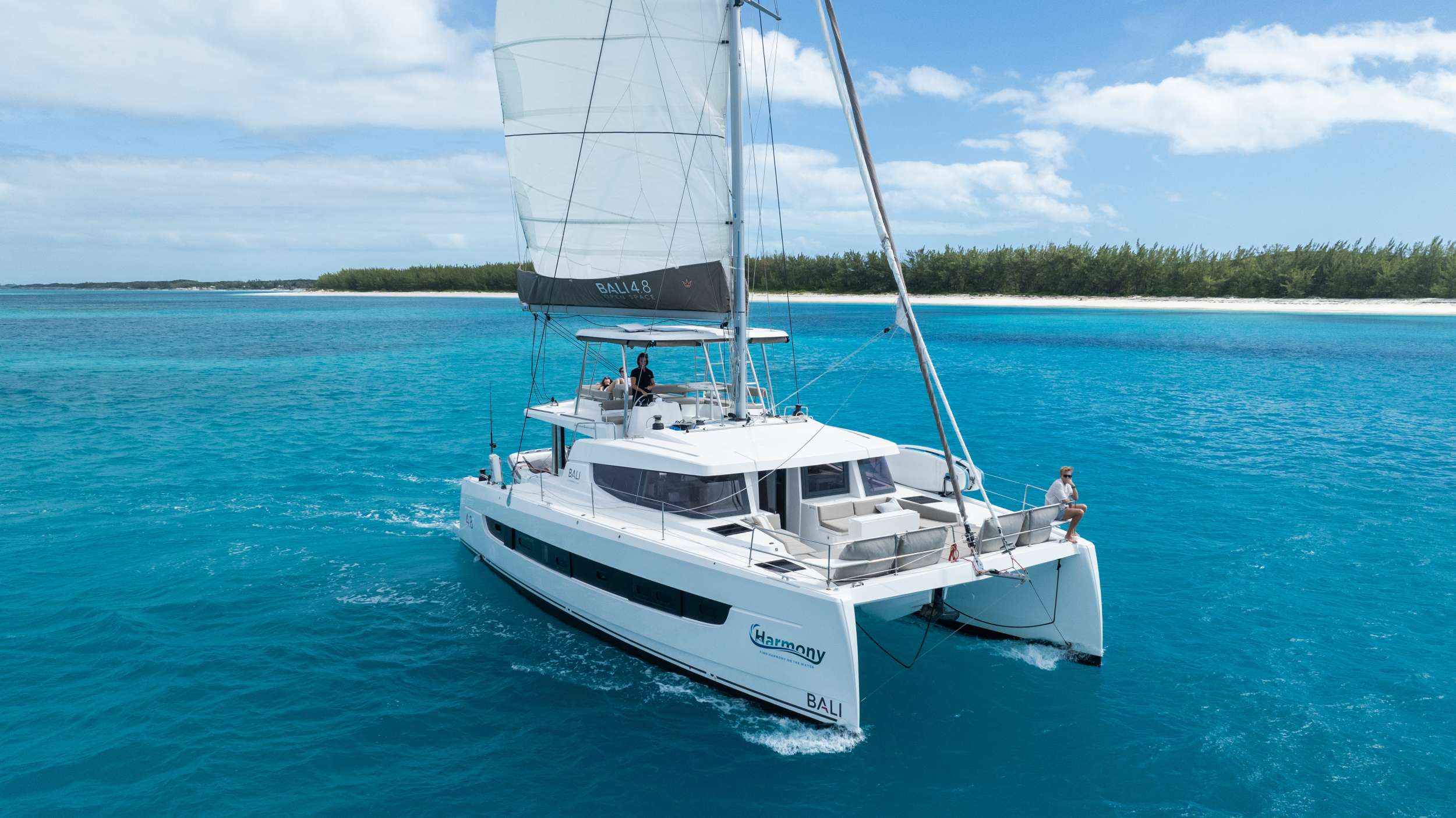 The Bali 4.8 design was new to the market in 2020 and provided a fresh approach to sailing. The design is revolutionary in how space is accessed, with deliberate attention to flow and open space. It succeeds in producing a scale that feels less like a boat, and more like an upscale floating condominium.

Bali catamarans are known and appreciated for their unparalleled success in blending luxury, space, and performance; producing a sailing experience that is unparalleled. This new design further capitalizes on that reputation with the advent of the “Bali garage door” that is the centerpiece of the yacht. It allows for the aft wall of the yacht to simply disappear, opening up the back of the yacht to an unobstructed view of paradise. This also affords indoor/outdoor dining options and gives the ever-present Bahamas breeze ample opportunity to make its way through the yacht with ease.

With her solid foredeck gone are the forward trampolines, replaced by a large relaxing lounge area complete with cushions for sunbathing. A full-sized door provides access directly from the lounge area into the salon, allowing free movement through the yacht. A walk up to the flybridge unveils a seating area perfect for cocktails and taking in sunsets. There is also another area for sunbathing on the flybridge where you can take in the sights of the islands from the highest vantage point on the yacht.

The Bali open space design is further complimented by the superior outfit of Harmony. No detail has been left unnoticed from the fine linens, pillows and throws to the wine glasses, serving and flatware that make every day feel luxurious. She has been stocked full with every appliance and kitchen accessory to allow the chef to fully showcase the mastery of their art. And the water toys abound, allowing guests to fully experience all the Bahamas has to offer, both in and out of the water.

Harmony will accommodate 8 charter guests in 4 spacious queen cabins. She has solar panels, air conditioning, water maker, ice maker, full sized refrigerator, a fully customizable menu, Caribbean made ecofriendly and reef safe toiletries, a bar stocked to guest preference, coffee/espresso machine, rendezvous scuba diving, snorkeling gear, underwater scooters, subwing, stand up paddle board, towable water tube, 10 ft. floating dock, pool noodles, fishing gear, board and card games, television in the salon, Fusion 3 Bluetooth enabled sound system and Harmony branded giveaways. 