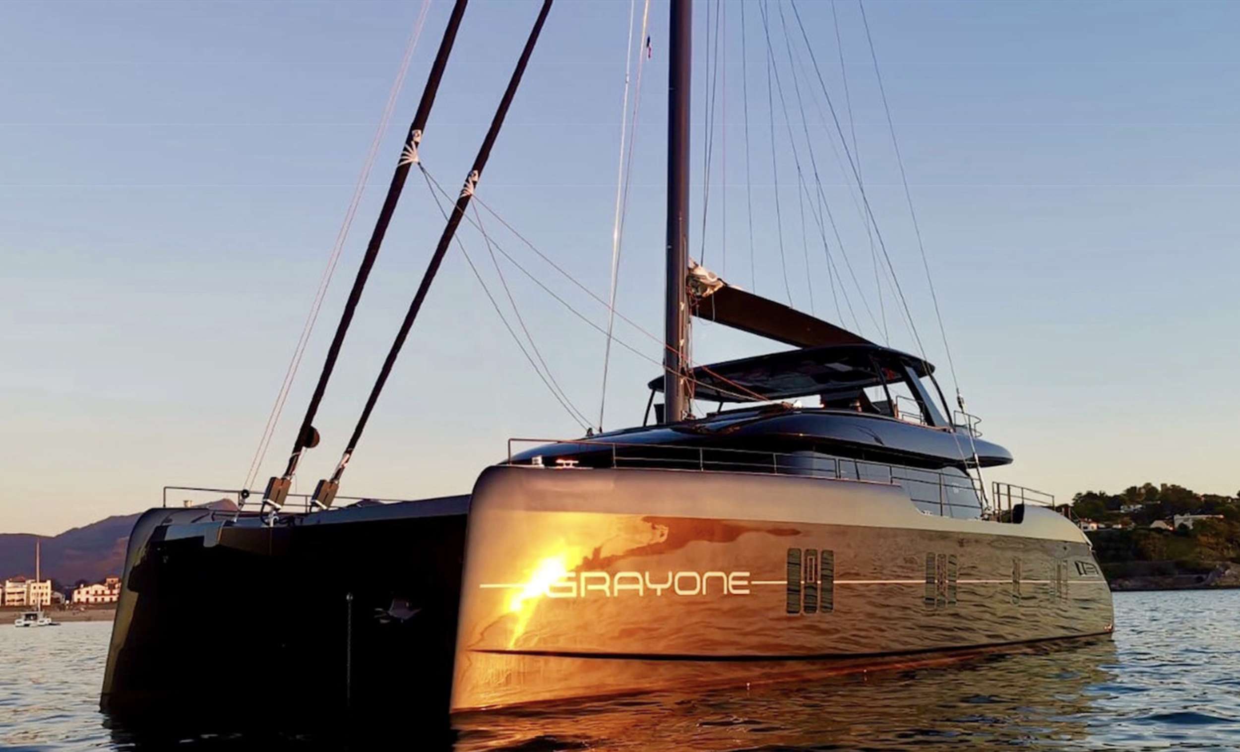 GRAYONE is a very fashionable dark grey hull color highlighting her gorgeous exterior lines and the enormous deck area covering the three teak decks. The formal dining area is located to port, while a luxurious sofa and matching drop-down table are located in the centre area, beneath the port windows. The opposite side features a comfy L-shaped sofa accompanied by coffee tables, armchairs, and footstools, all of which can be used as extra gathering and resting spaces. In contrast to the traditional nautical decor found on other luxury yachts of a comparable size, the interior of this one features a light ceiling and floors, dark blue and white tones, and a warm, welcome soft orange utilized in part for the materials.
The GRAYONE luxury catamaran's clever internal layout allows for a front bar complete with a wine cellar to serve guests both inside the boat and on the foredeck. Guests will have a hard time deciding between the aft cockpit, the spacious flybridge, and the upper deck, which features two loungers, integrated seating with breathtaking views of the water, and a cocktail table.
A wide electro-hydraulic bathing platform is essential for the luxury crewed catamaran GRAYONE to store the fast tender, which is powered by 110hp and can reach speeds of over 35 knots. Along with the floating deck, the water toys, which include water skis, and a 16-square-meter floating swimming pool, may be securely thrown into the water.